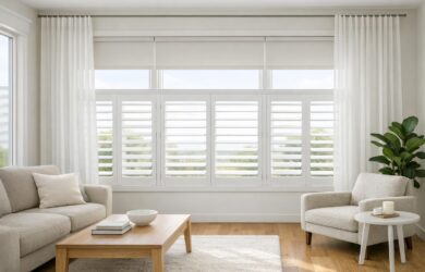 A bright, modern living room with large windows featuring allergy-friendly roller shades, plantation shutters, and sheer drapery in a clean, dust-free environment.